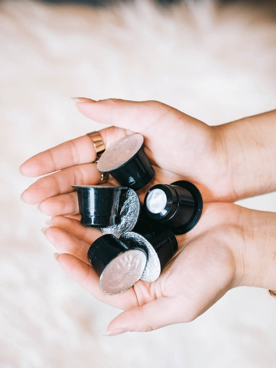 A women's hands holding 6 black coffee capsules. 