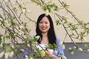 Jenny Tan holding a cup of coffee underneath a flowering tree